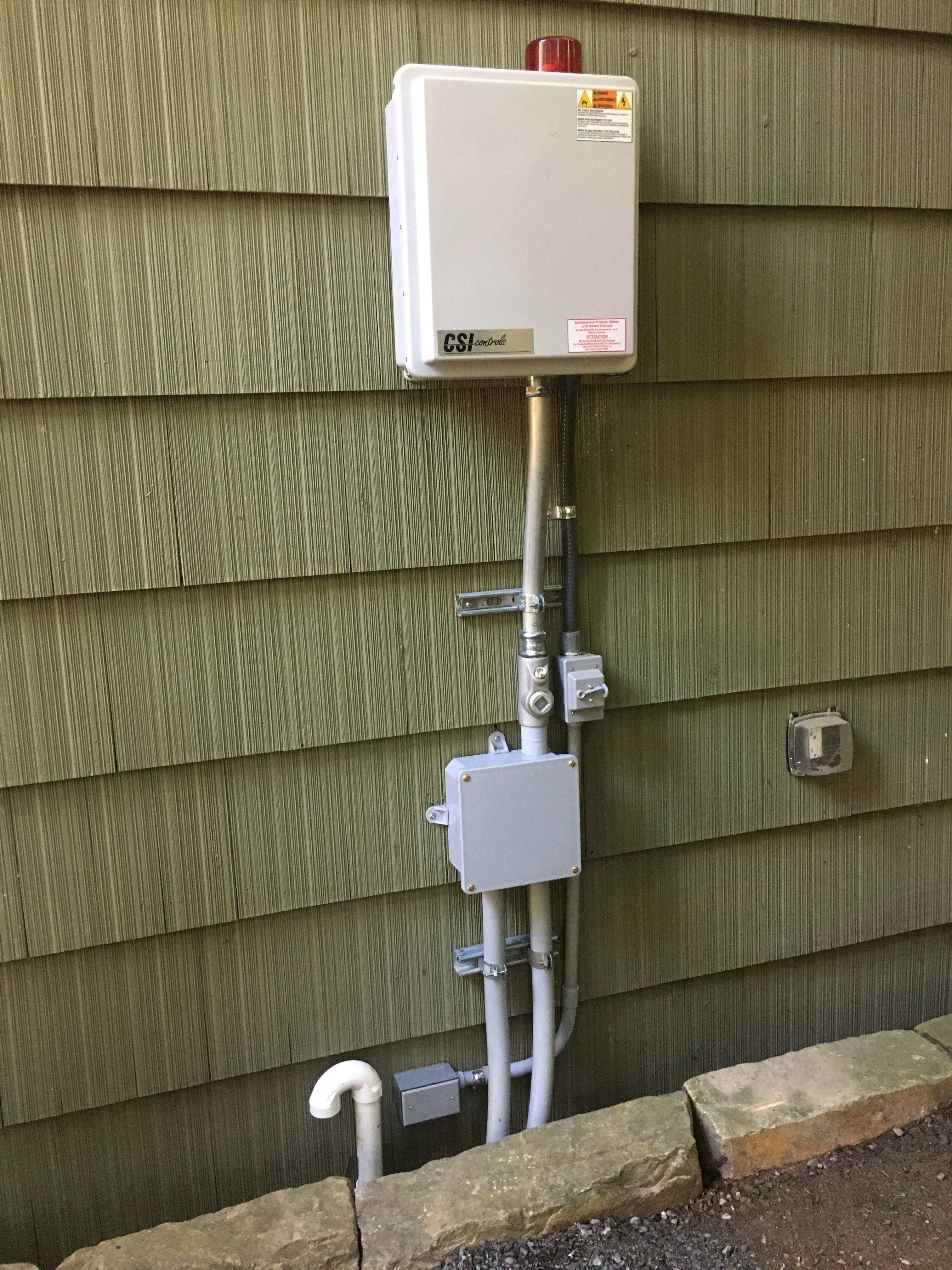 A grinder pump control panel and warning alarm mounted to the side of a home.
